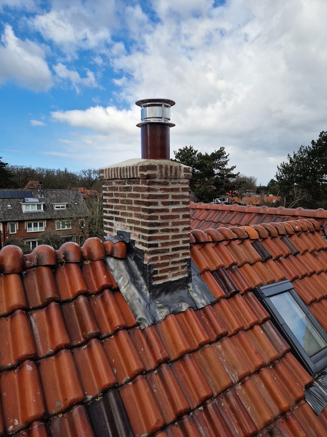 Gerenoveerde gemetselde schoorsteen met nieuwe kap op een rood pannendak.